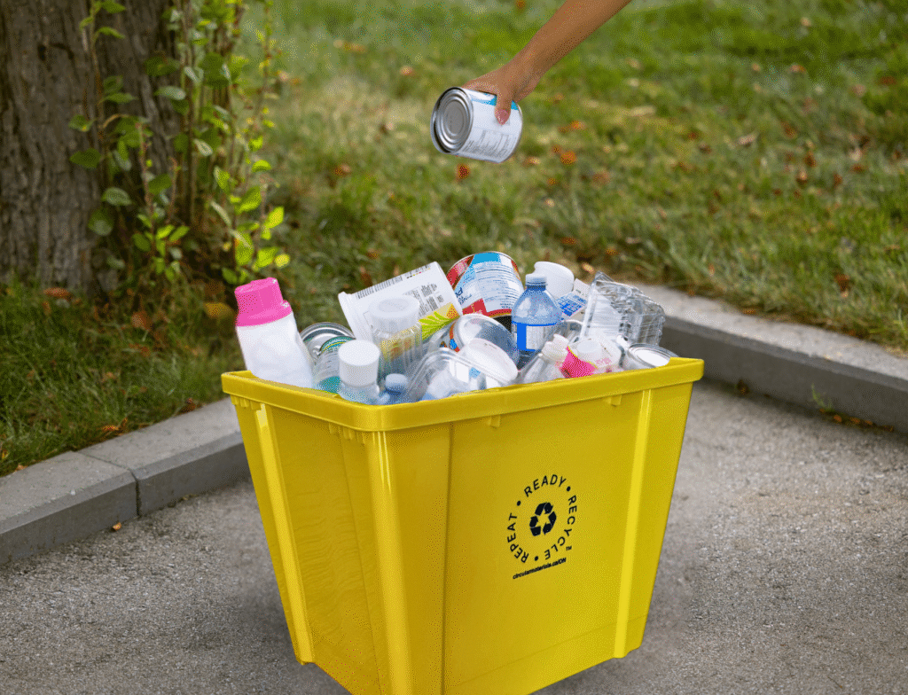 image of gold recycling box with materials inside and a hand placing a metal container in it