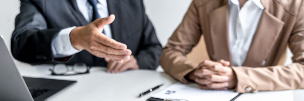photo of two people sitting at a board room table with one hand held out for handshake