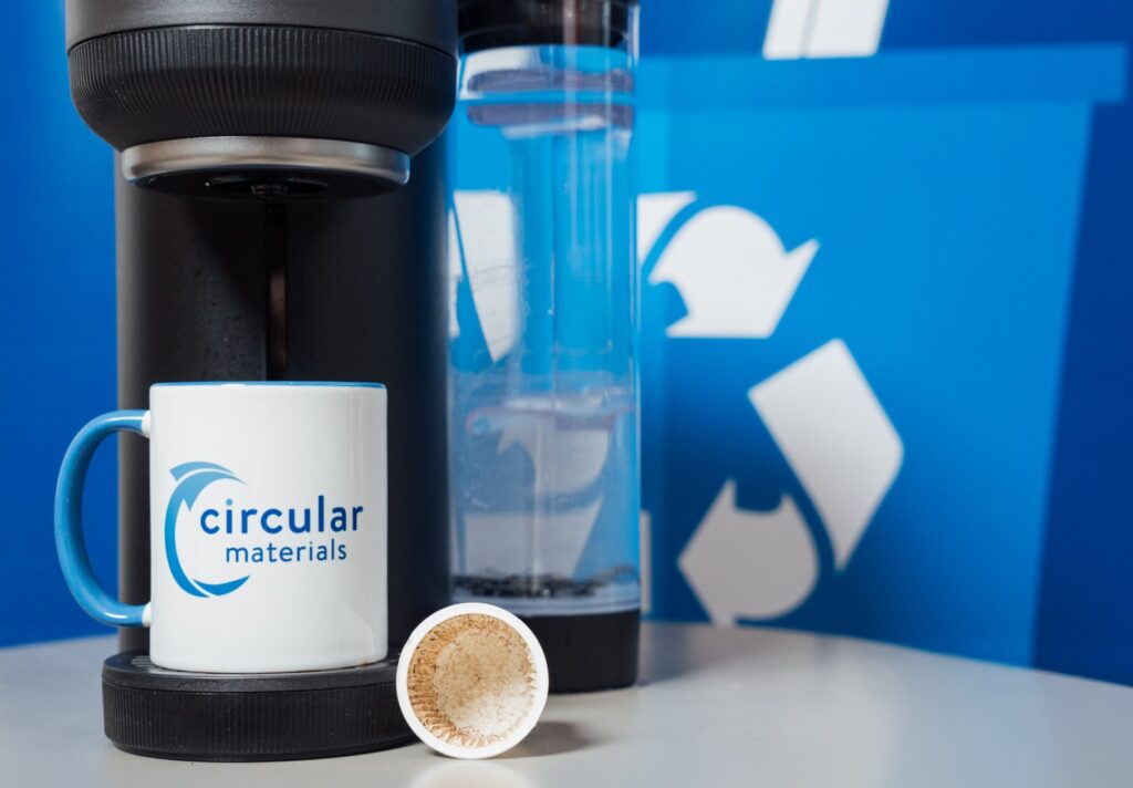 Keurig coffee pod with Circular Materials branded coffee mug against blue recycling bin background